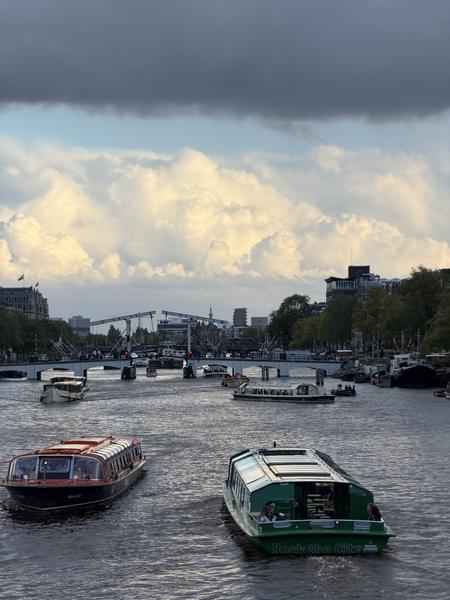 This photo captures a serene view of the Amstel River at Blauwbrug, Centrum, Amsterdam, under a dramatic cloudy sky